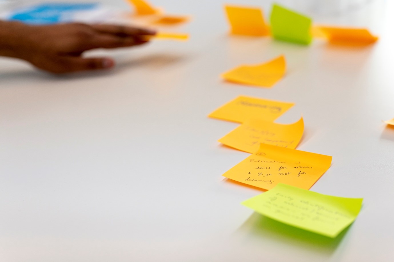 Close-up of a row of different colour post-it notes and the hand of someone writing on them