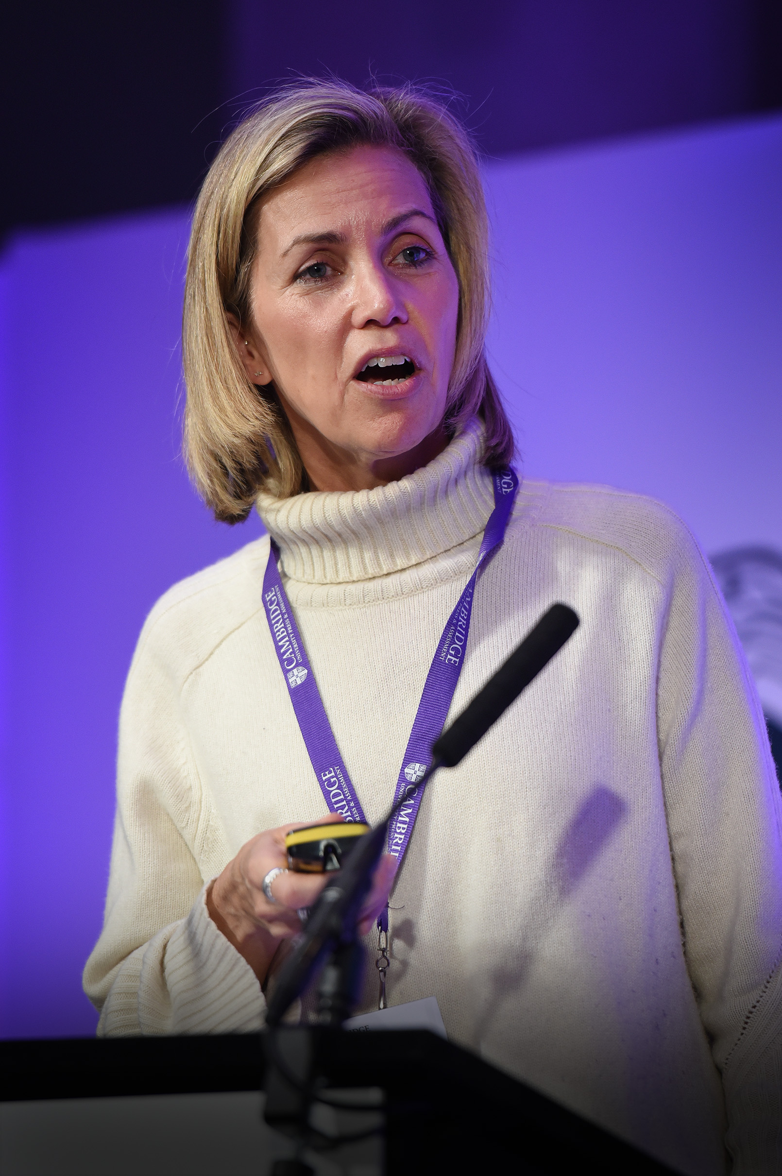 Julie Dennis wearing a cream white jumper holds a remote and speaks into a mic on stage delivering her keynote speech at Digital & Data Day