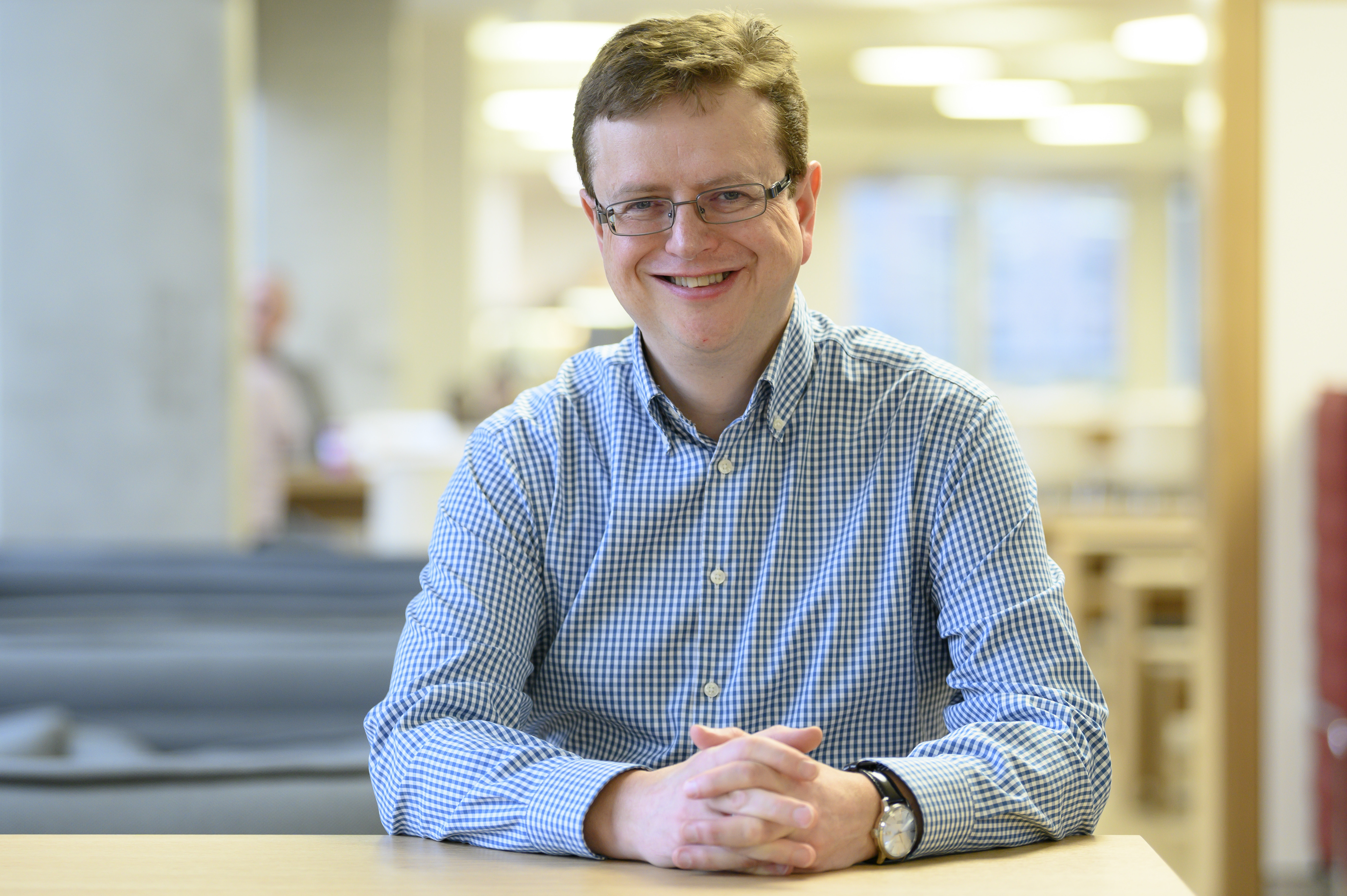 Nick Raikes, Assistant Director of Research, Data Science Unit at Cambridge University Press & Assessment, smiles for a headshot while wearing a blue and white chequered shirt 