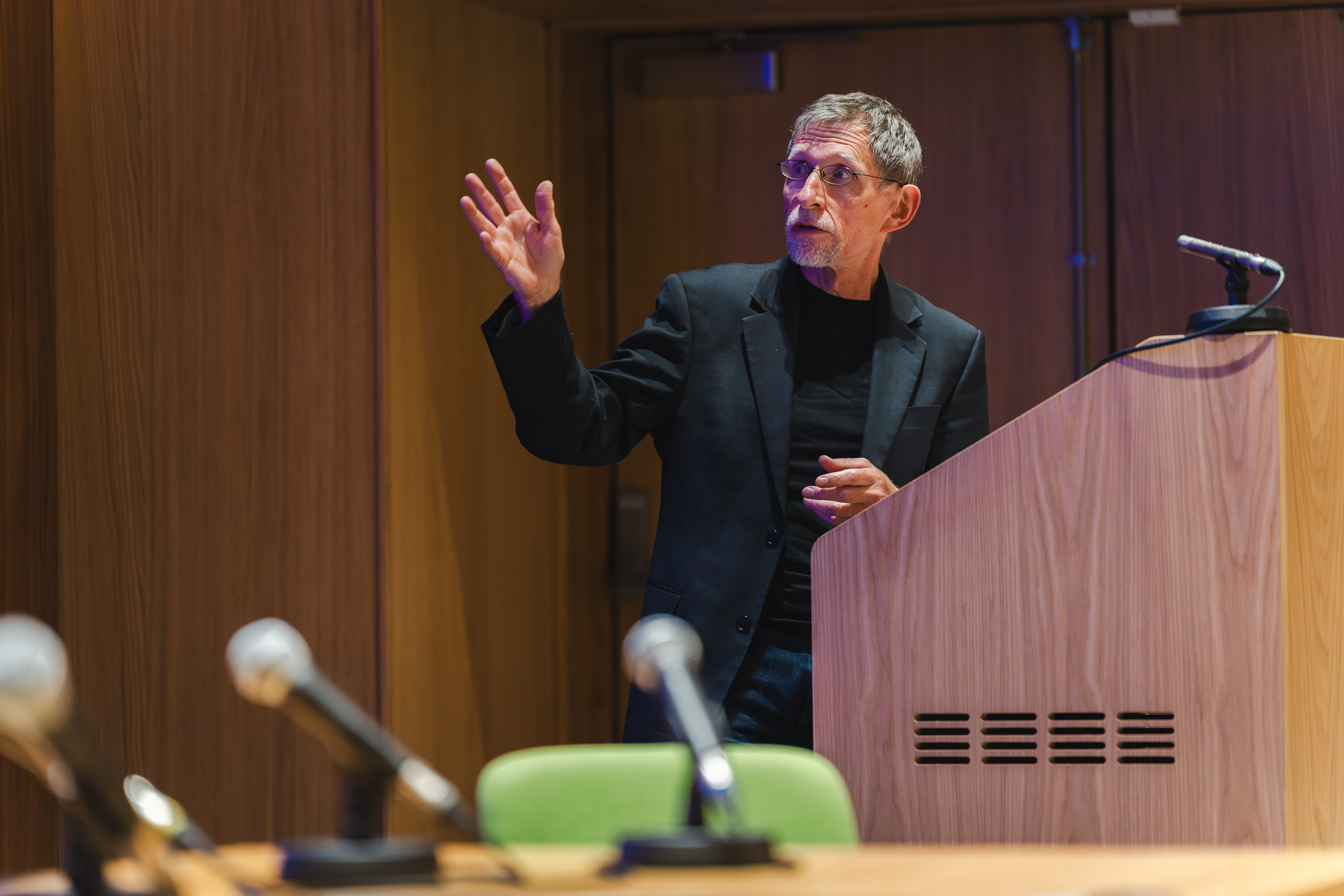 Tim Oates stands at a lectern pointing towards his presentation: 'Human elements of digital learning and assessment applications'