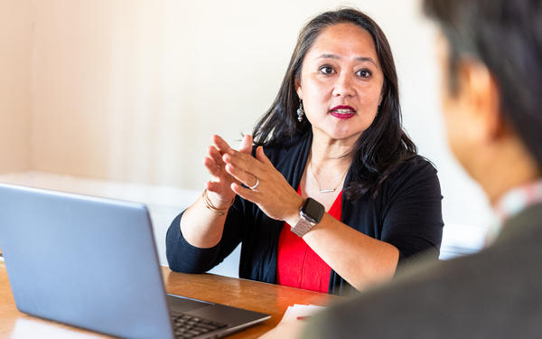 two people in a workplace are sat in front of a laptop discussing a topic