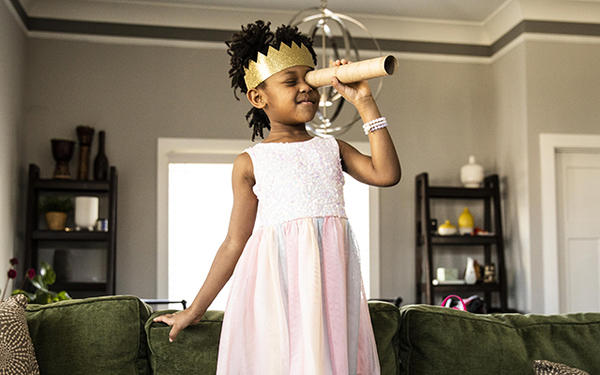 young girl wearing a toy crown looking through a homemade telescope