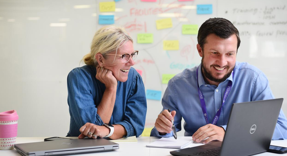 two Cambridge staff members smiling looking at a laptop screen