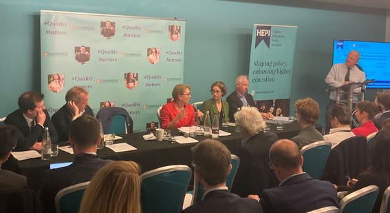 Pamela Baxter speaking at a panel table with four others, while attendees listen. Quality Matters signage and the Cambridge University Press & Assessment and HEPI logos are visible in the background.